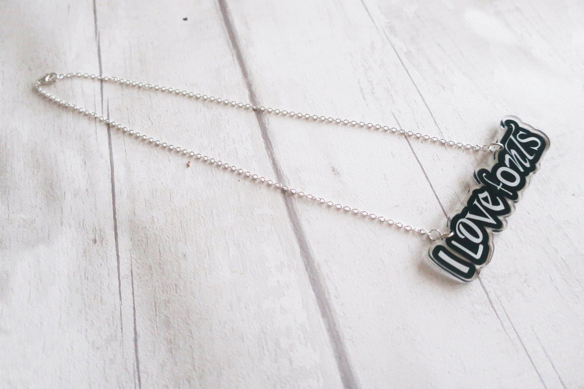Necklace with 'I LOVE FONTS' pendant on a light wooden surface