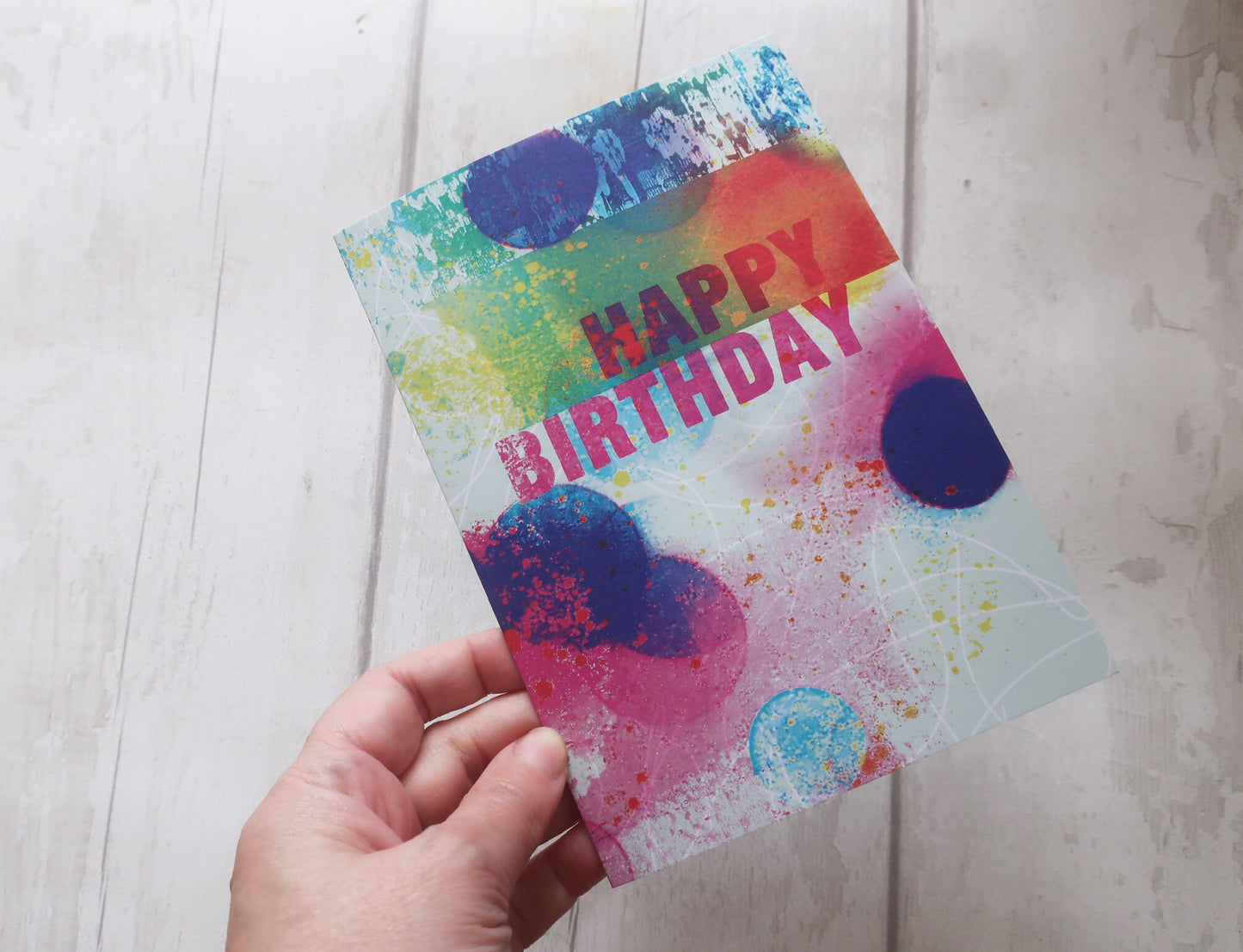 Colorful birthday card with abstract design held by a hand on a light wooden surface