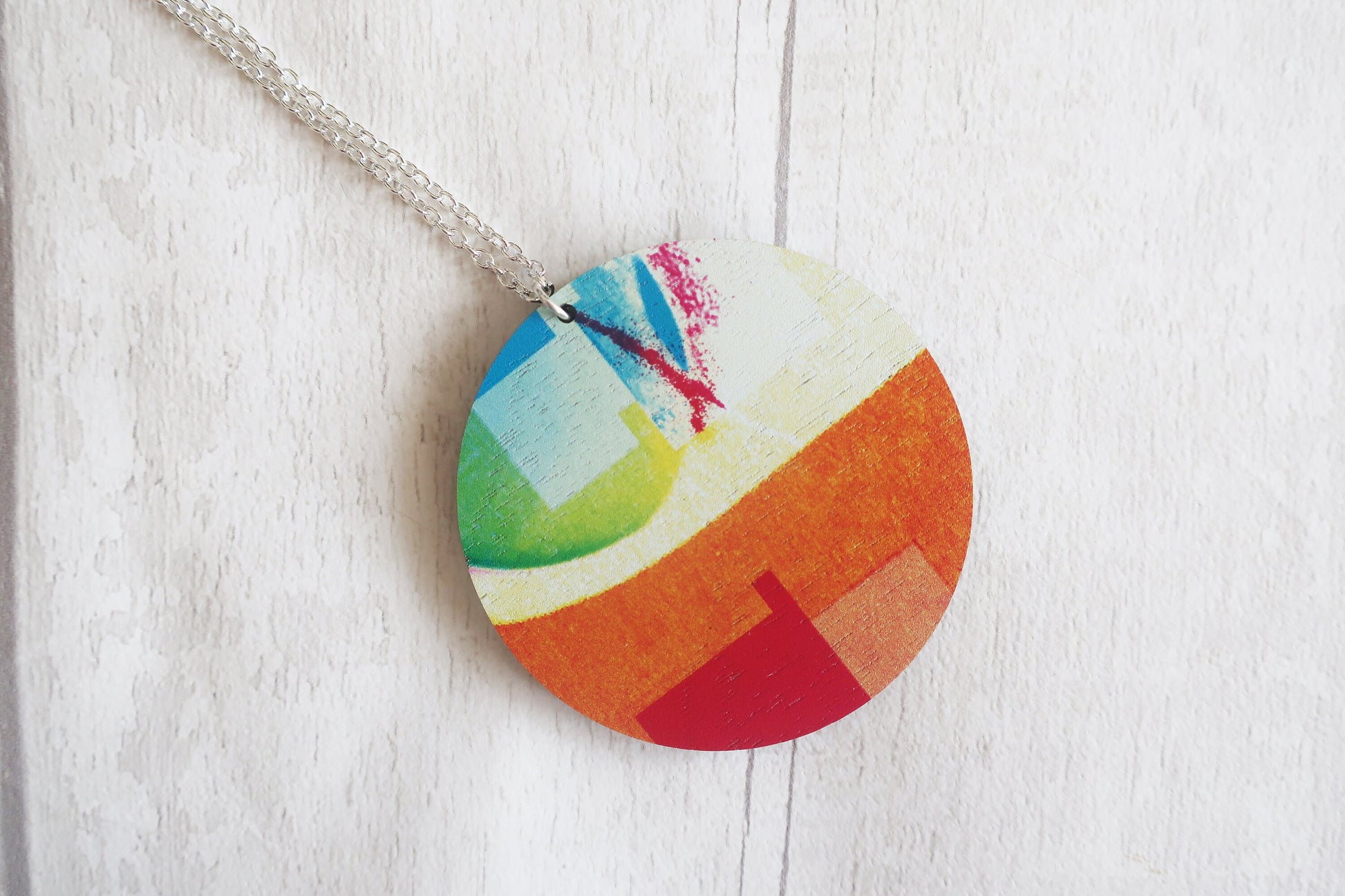 Colorful circular pendant on a chain against a white wooden background