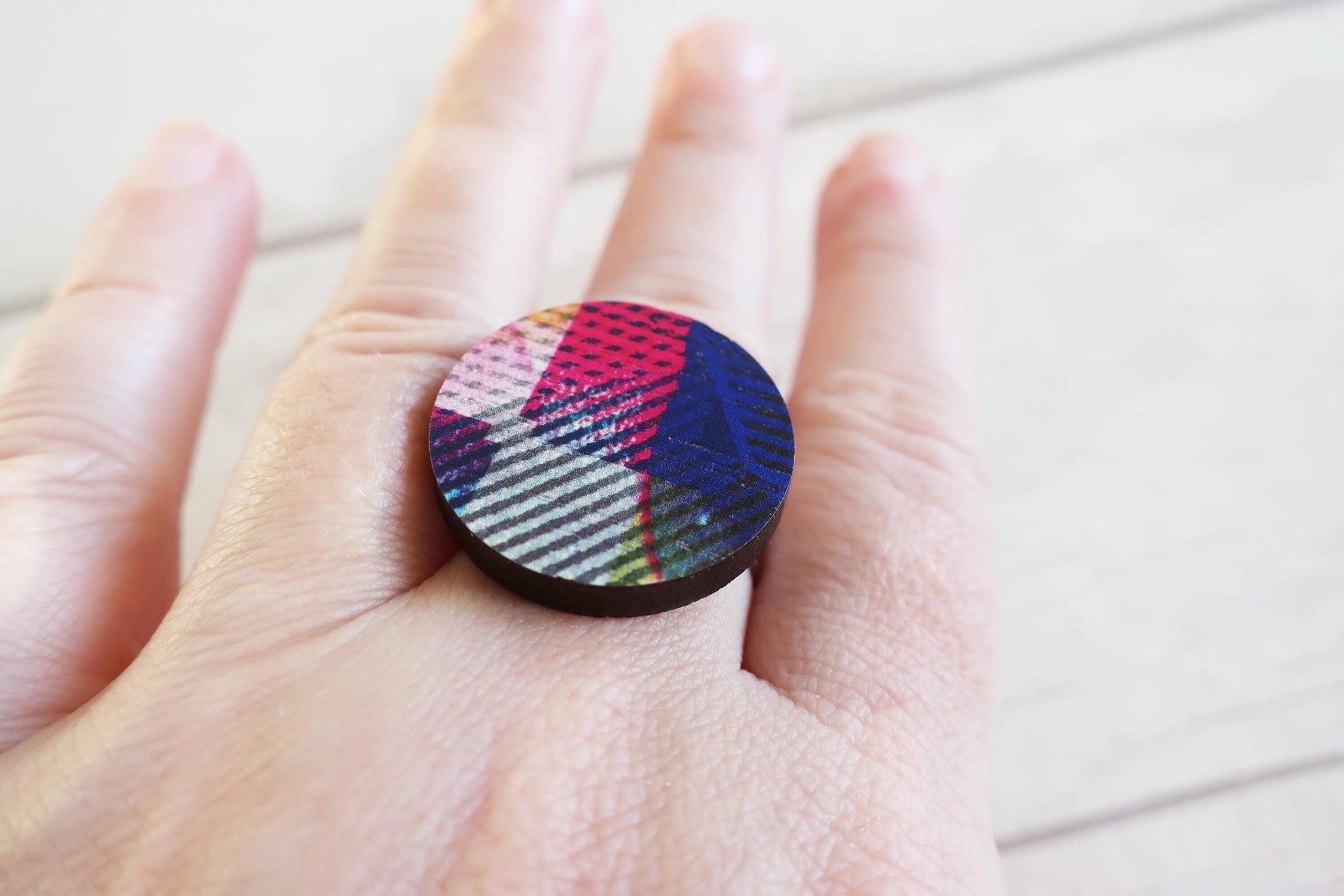 Hand wearing a colorful ring on a light background