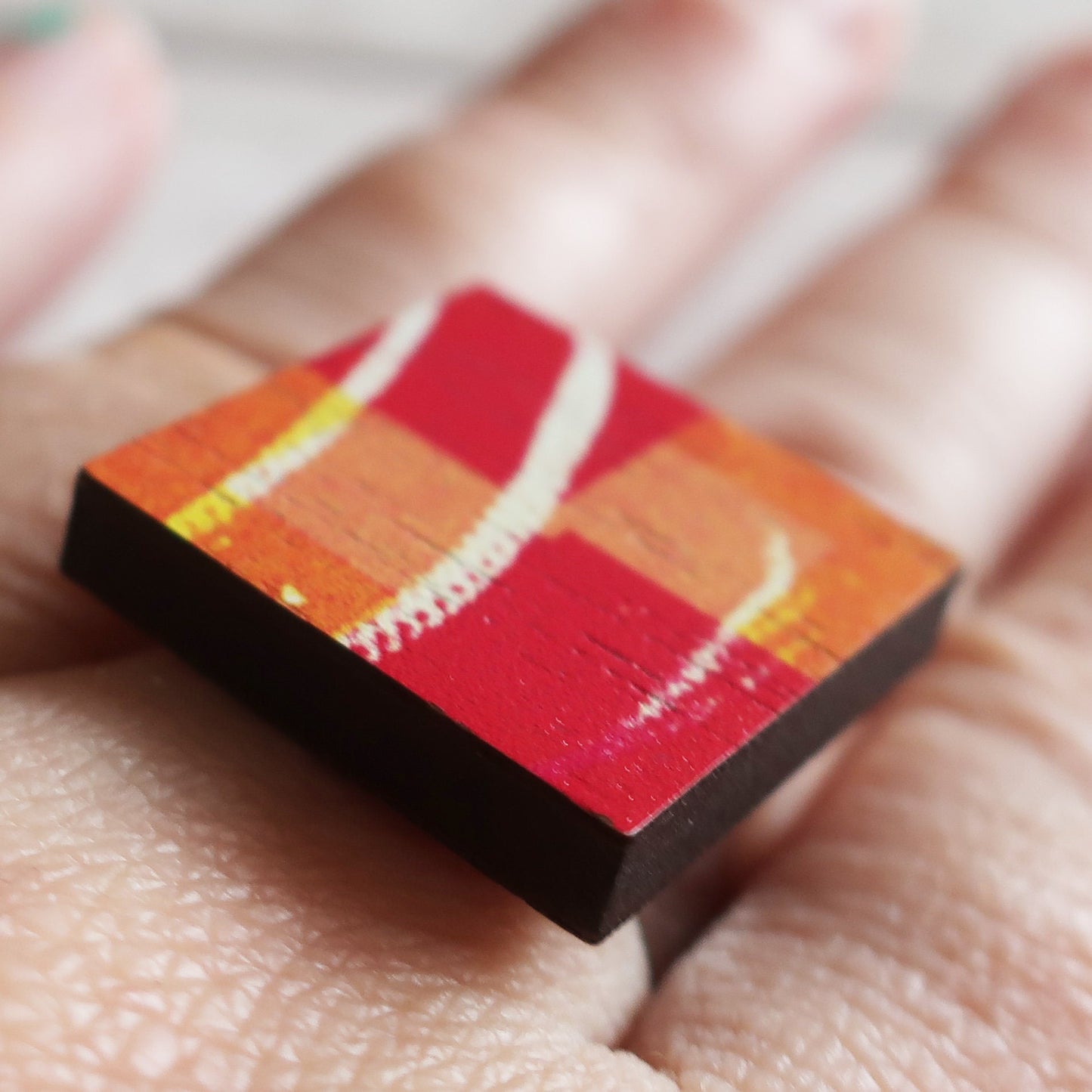 Small square wooden ring with a red and orange gradient held between fingers
