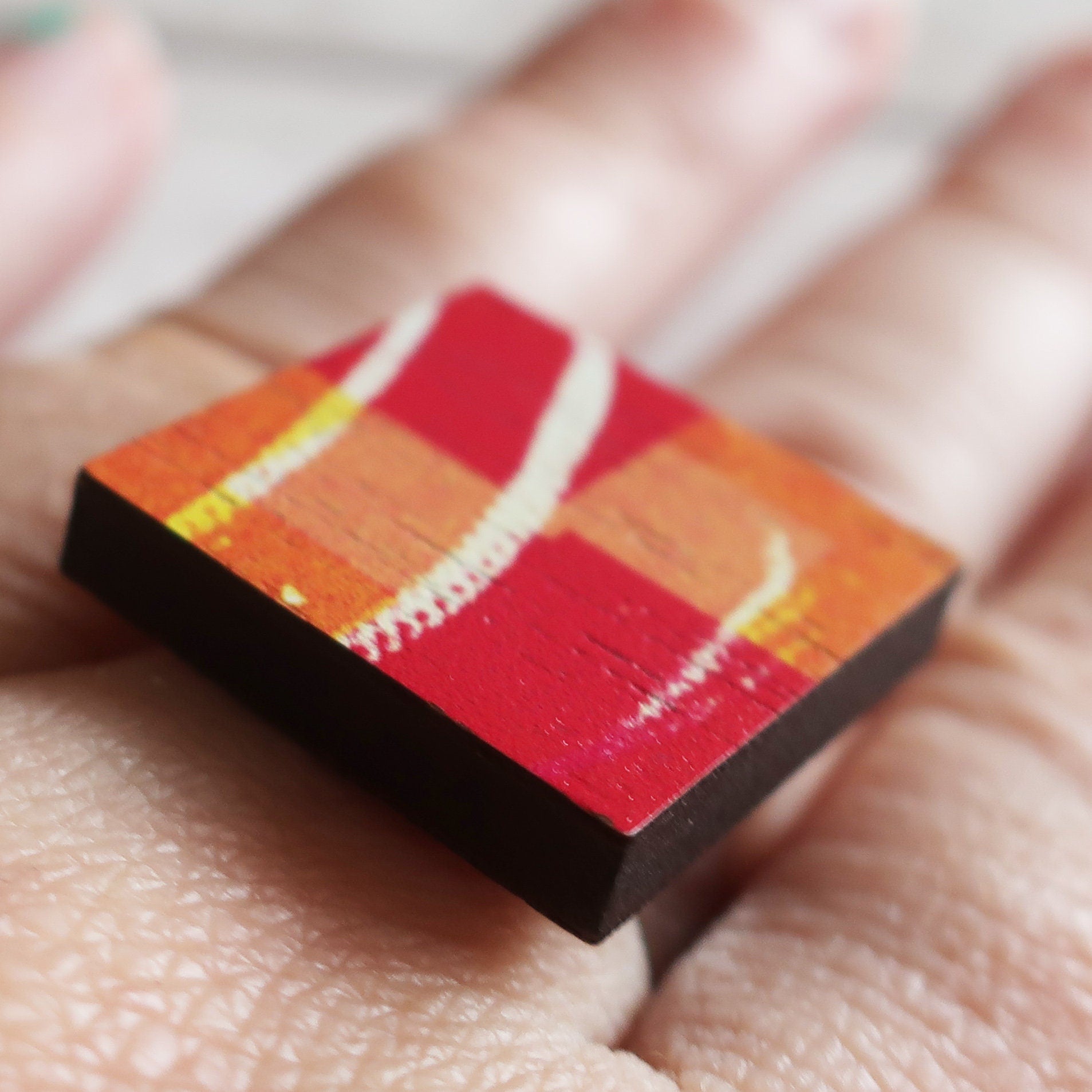 Small square wooden ring with a red and orange gradient held between fingers