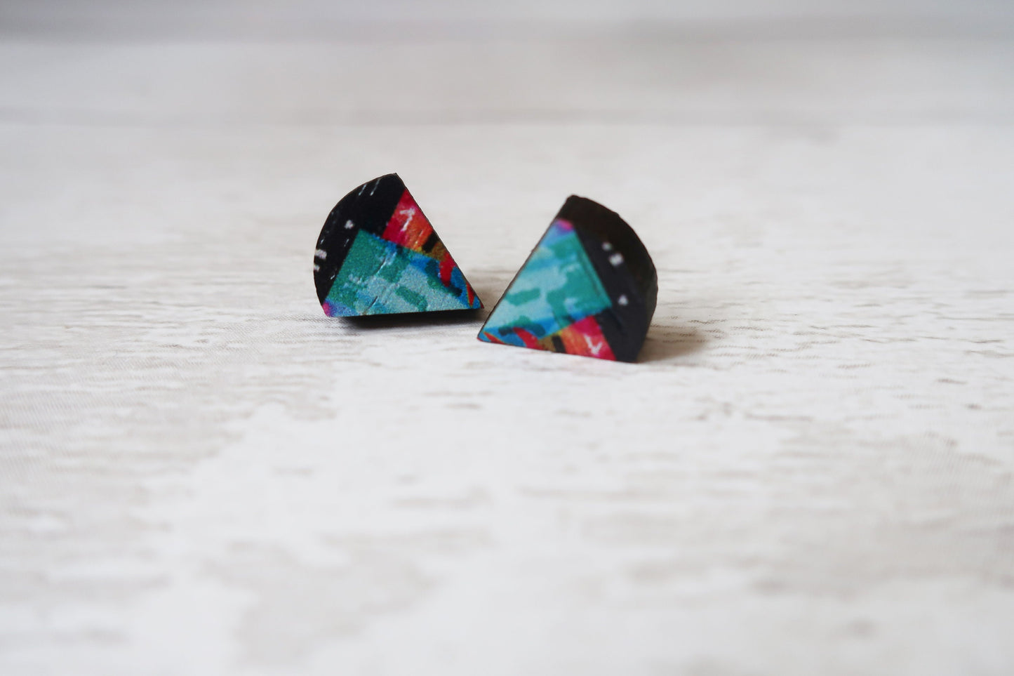 Triangular earrings with colorful designs on a light wooden surface