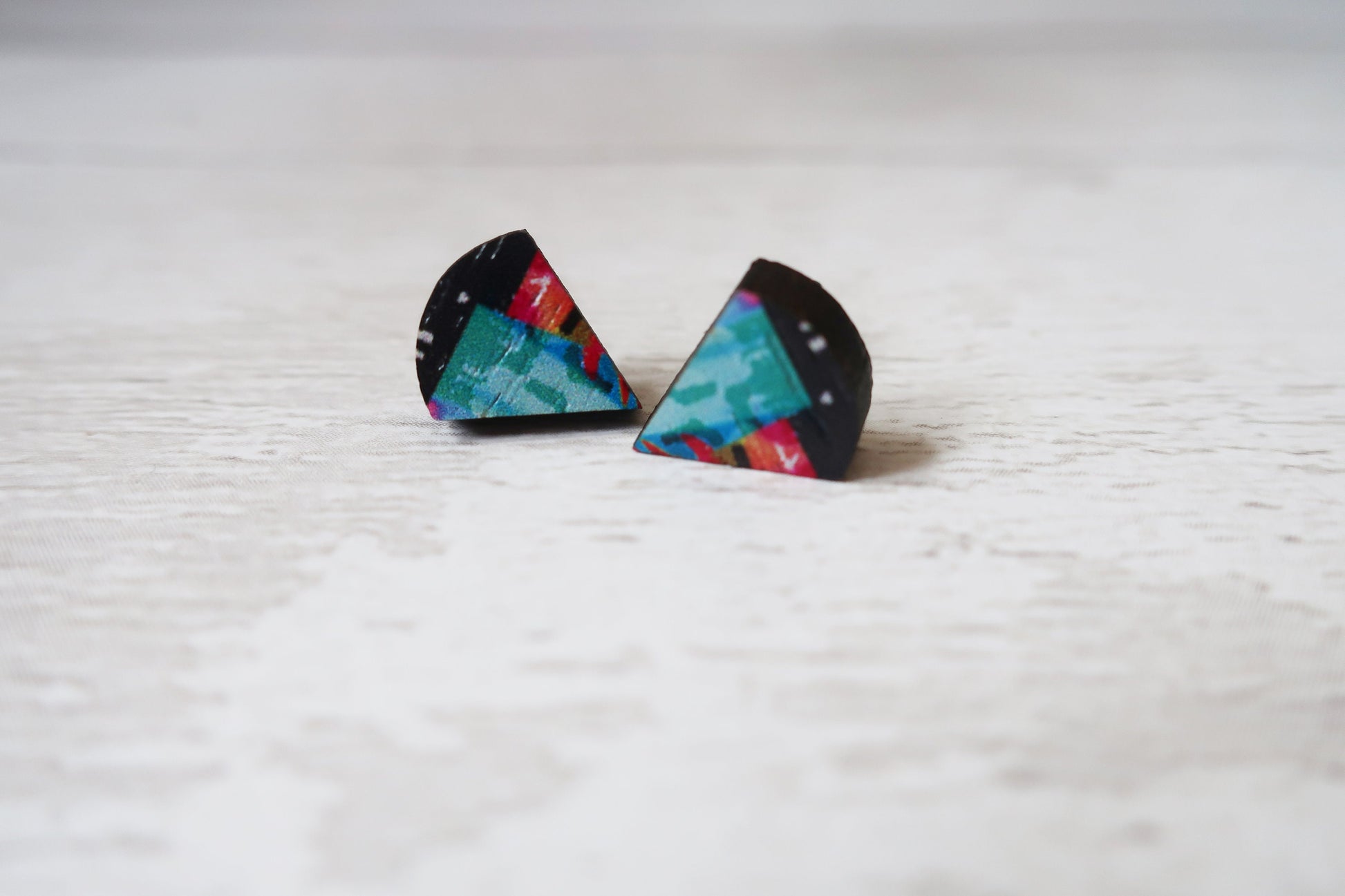 Triangular earrings with colorful designs on a light wooden surface