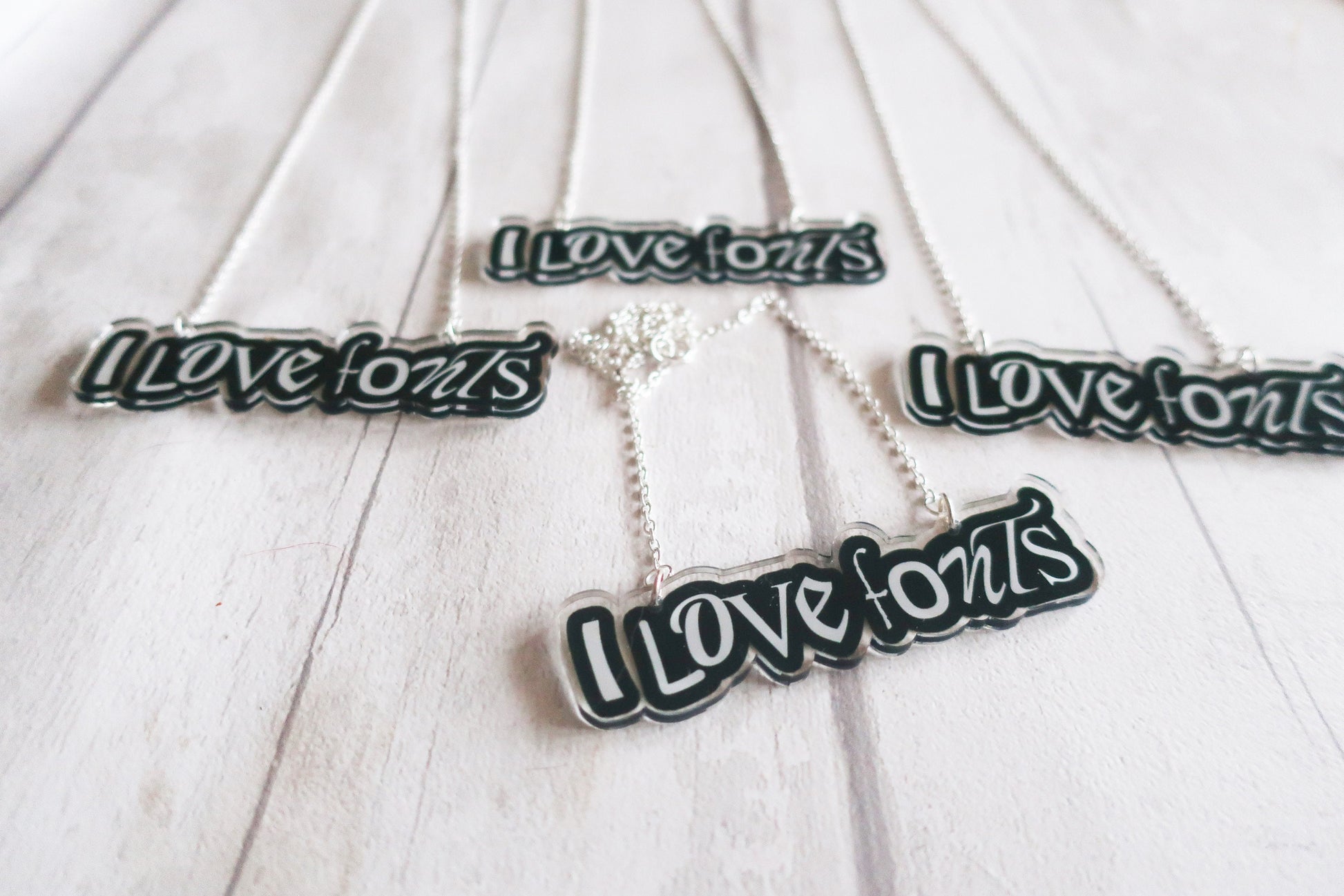 Silver necklaces with 'I love fonts' pendants on a white wooden surface