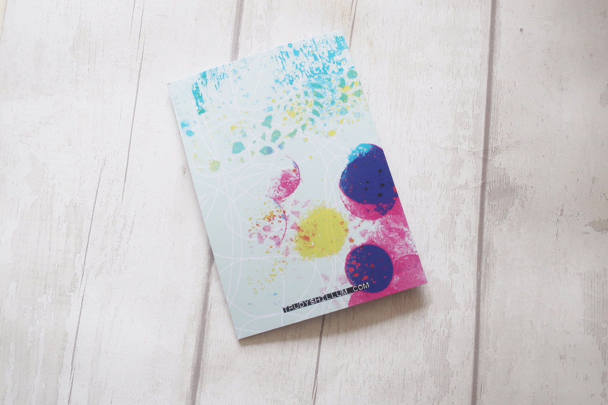 Colorful splatter-patterned back of card on a light wooden surface