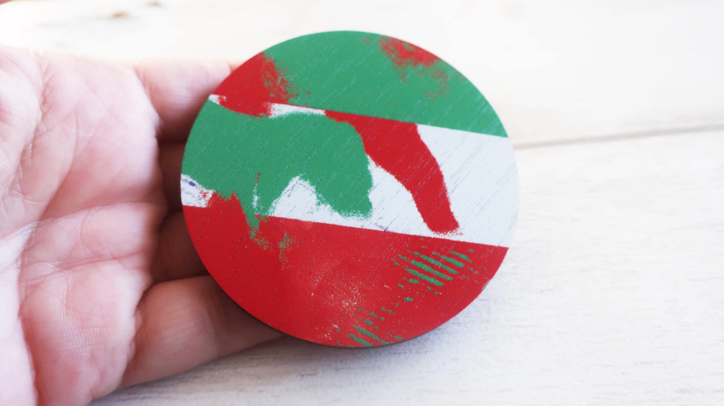 Round red, green, and white brooch held in a hand on a light background