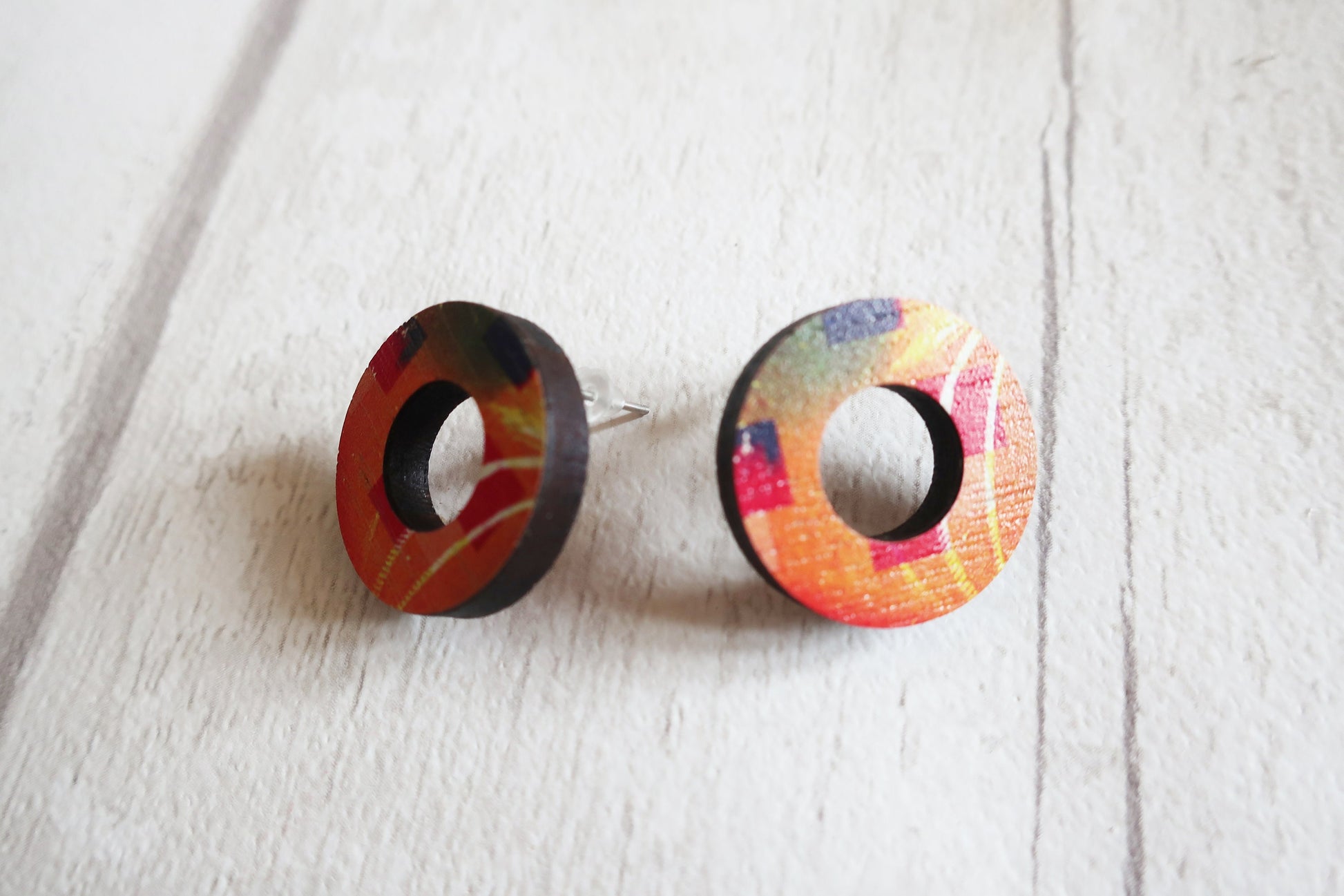 Pair of colorful round earrings on a white wooden surface