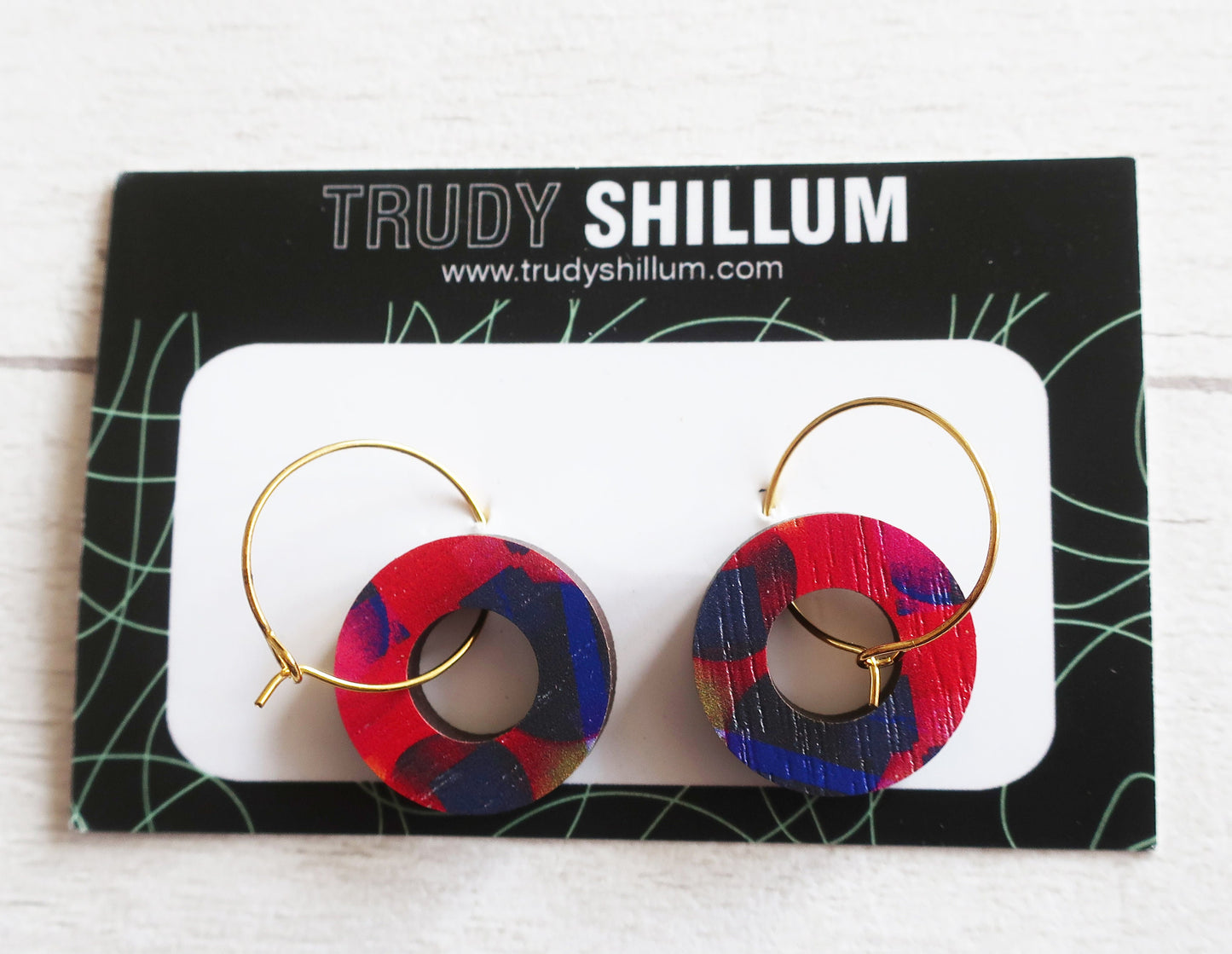 Red and blue hoop earrings on a Trudy Shillum branded card.