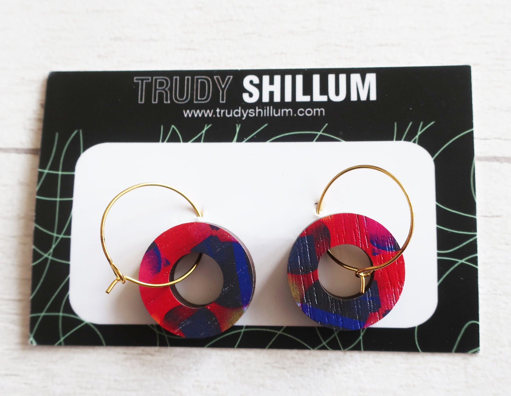 Red and blue hoop earrings on a Trudy Shillum branded card.