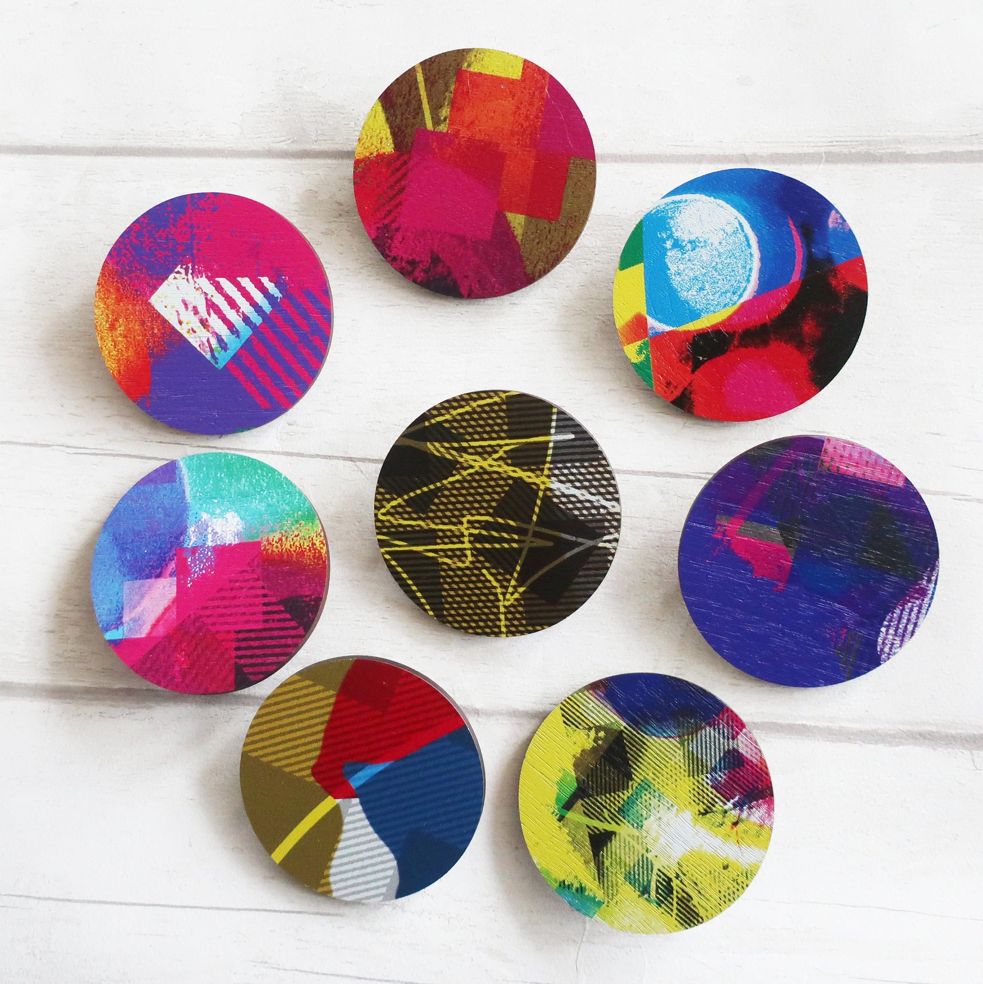 Set of colorful circular design brooches on a white wooden surface