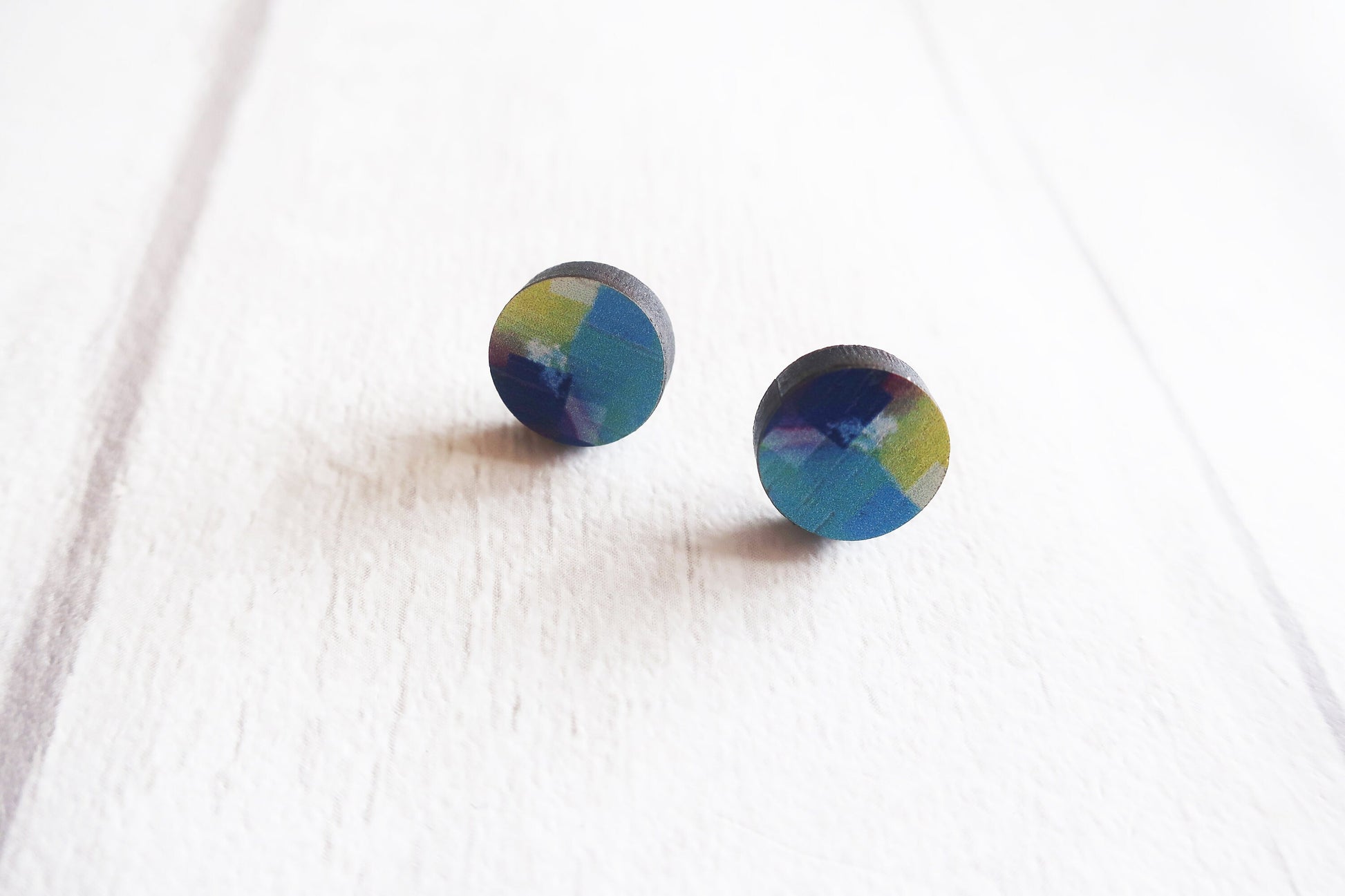 Pair of round earrings with a multicolored design on a white fabric background