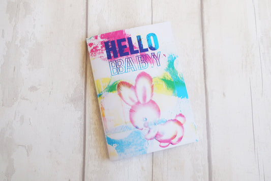 Greeting card  with a colorful bunny illustration and 'Hello Baby' text on a light wooden surface