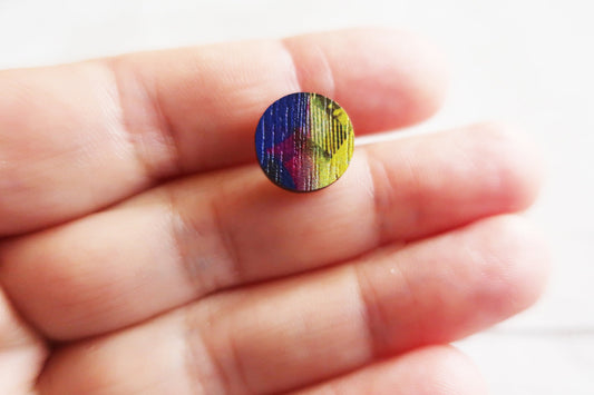 Small round earring  with a colorful pattern held between fingers against a blurred background