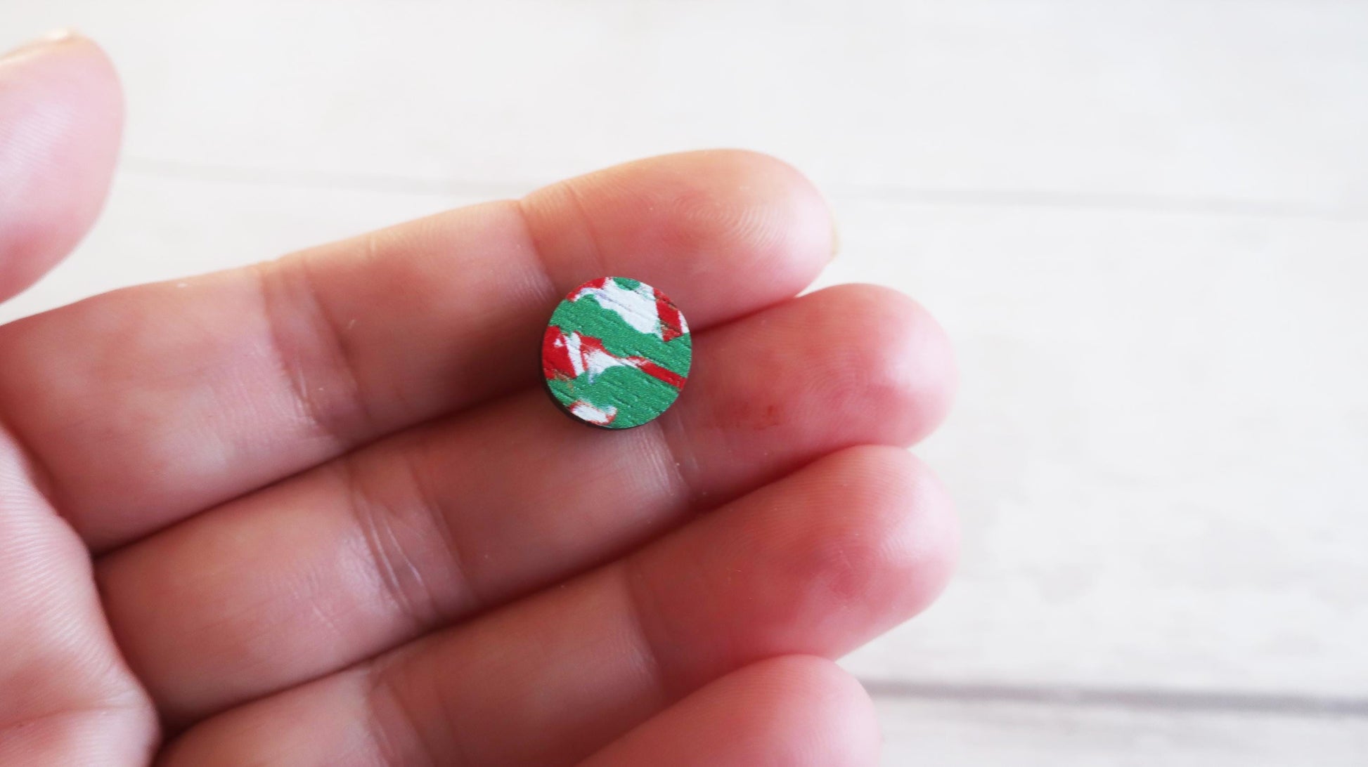 Small round earring with a colorful design held between fingers on a white background