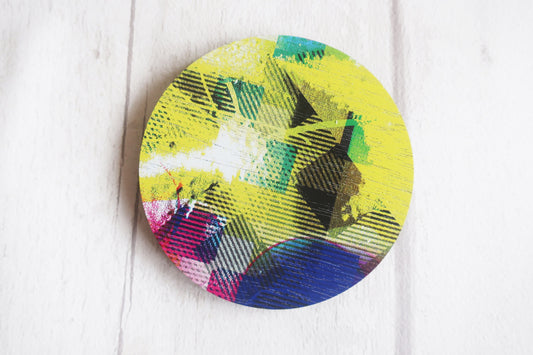 Colorful circular brooch with abstract design on a white wooden surface