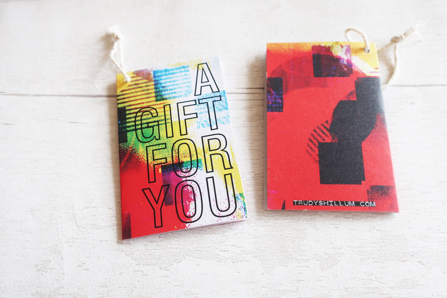 Two colorful gift cards hanging on a white wooden surface.