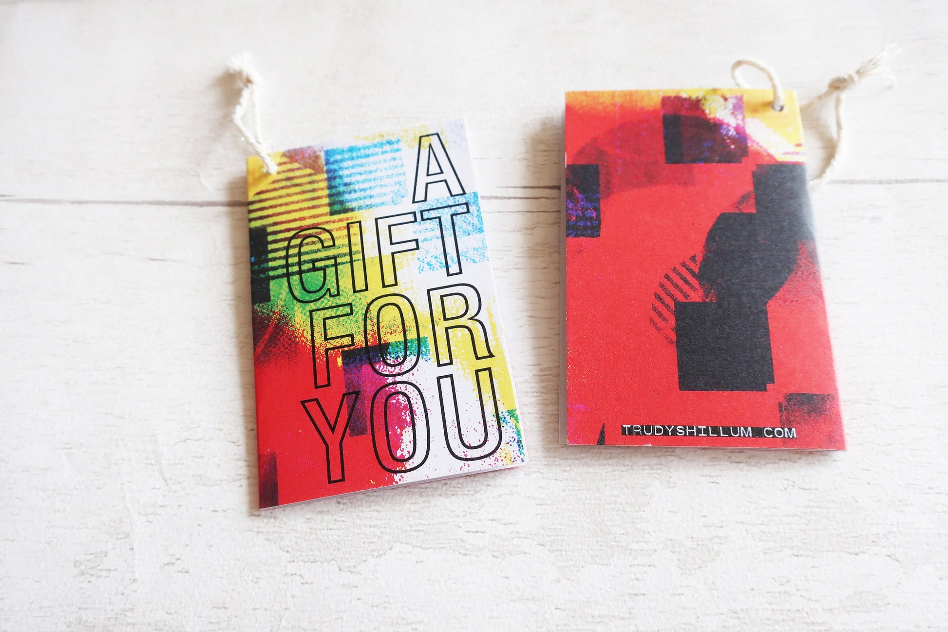 Two colorful gift cards hanging on a white wooden surface.