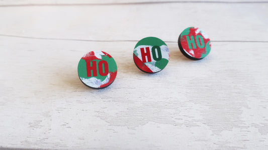 Three circular pin badges with 'HO' design on a light wooden surface