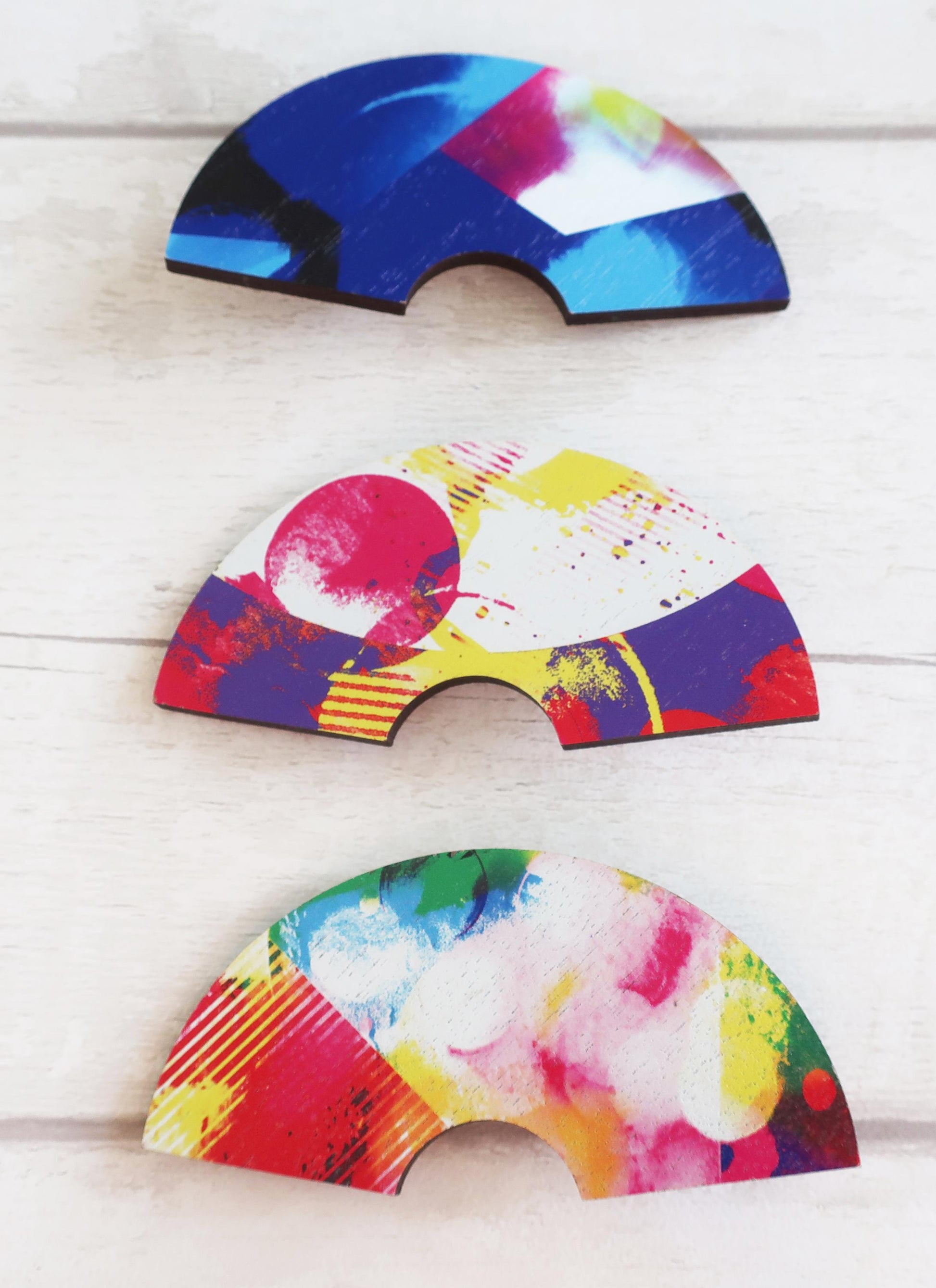 Three colorful half-circle hairclips on a light wooden surface