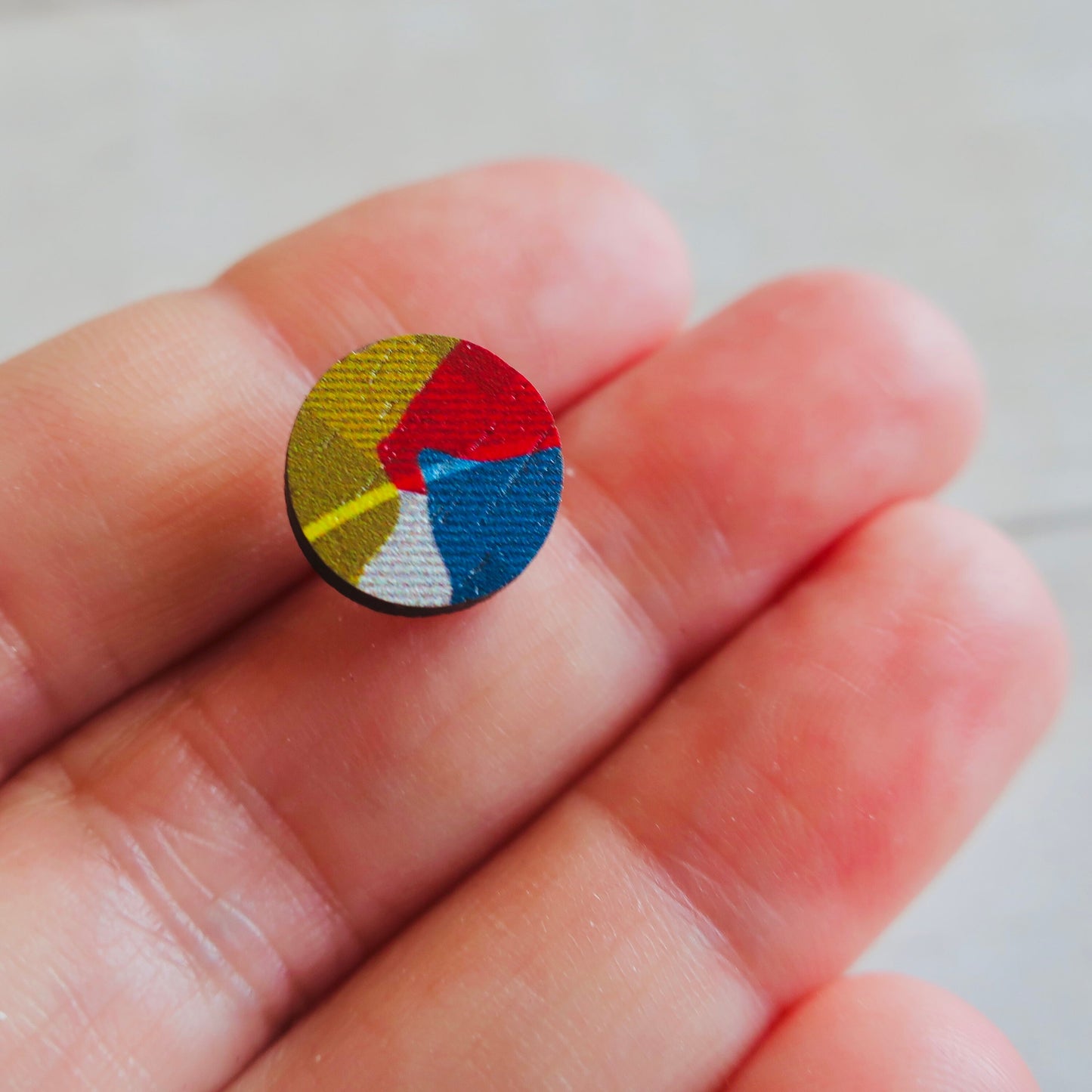 Colorful circular earring held between fingers against a neutral background