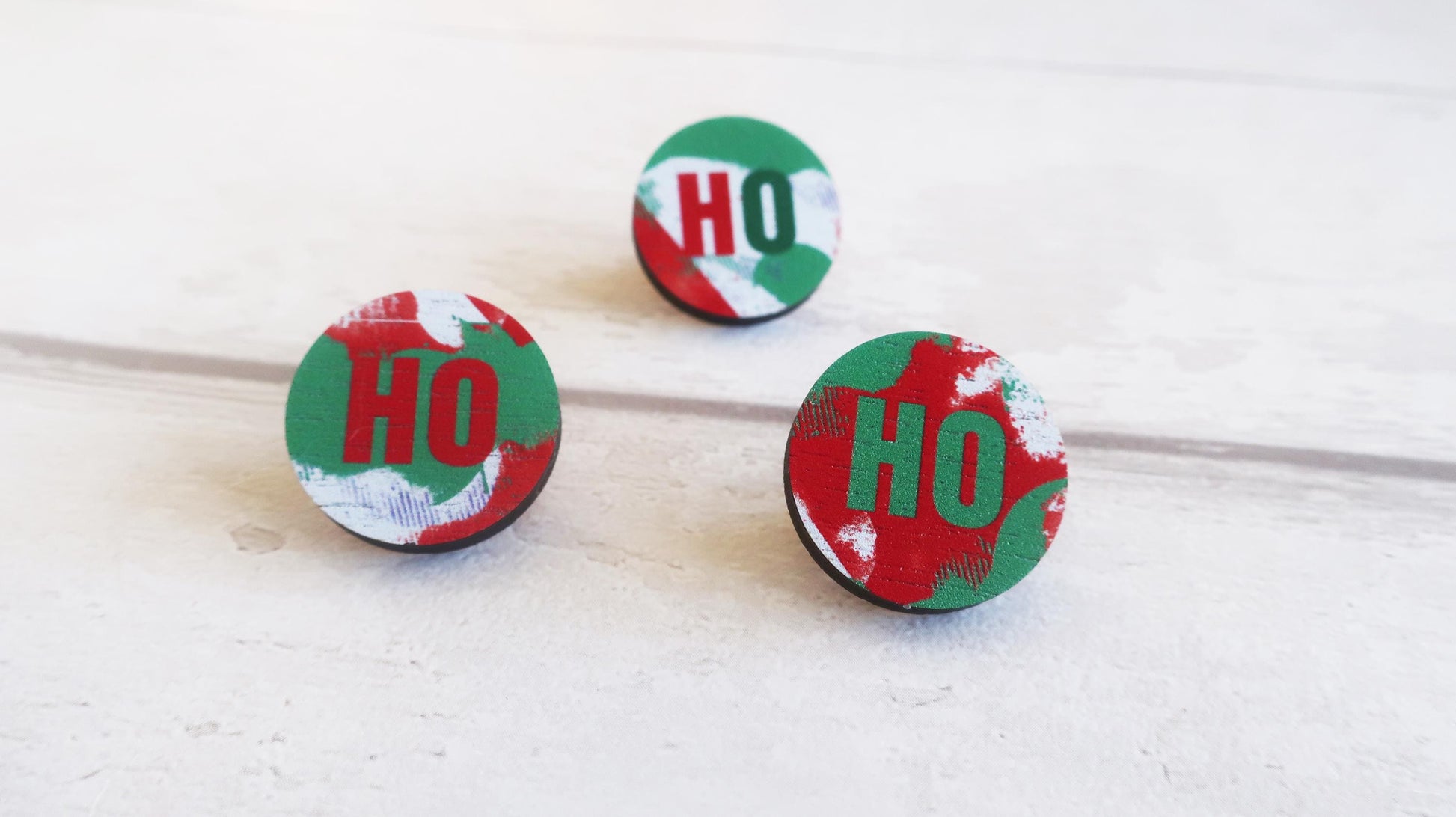 Three round Christmas-themed pin badges with 'HO' text on a white background
