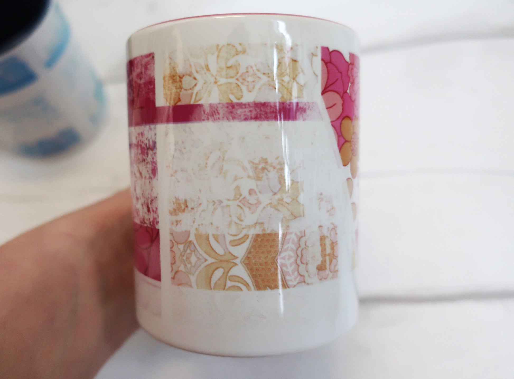 Ceramic mug with floral pattern held by a hand on a white background