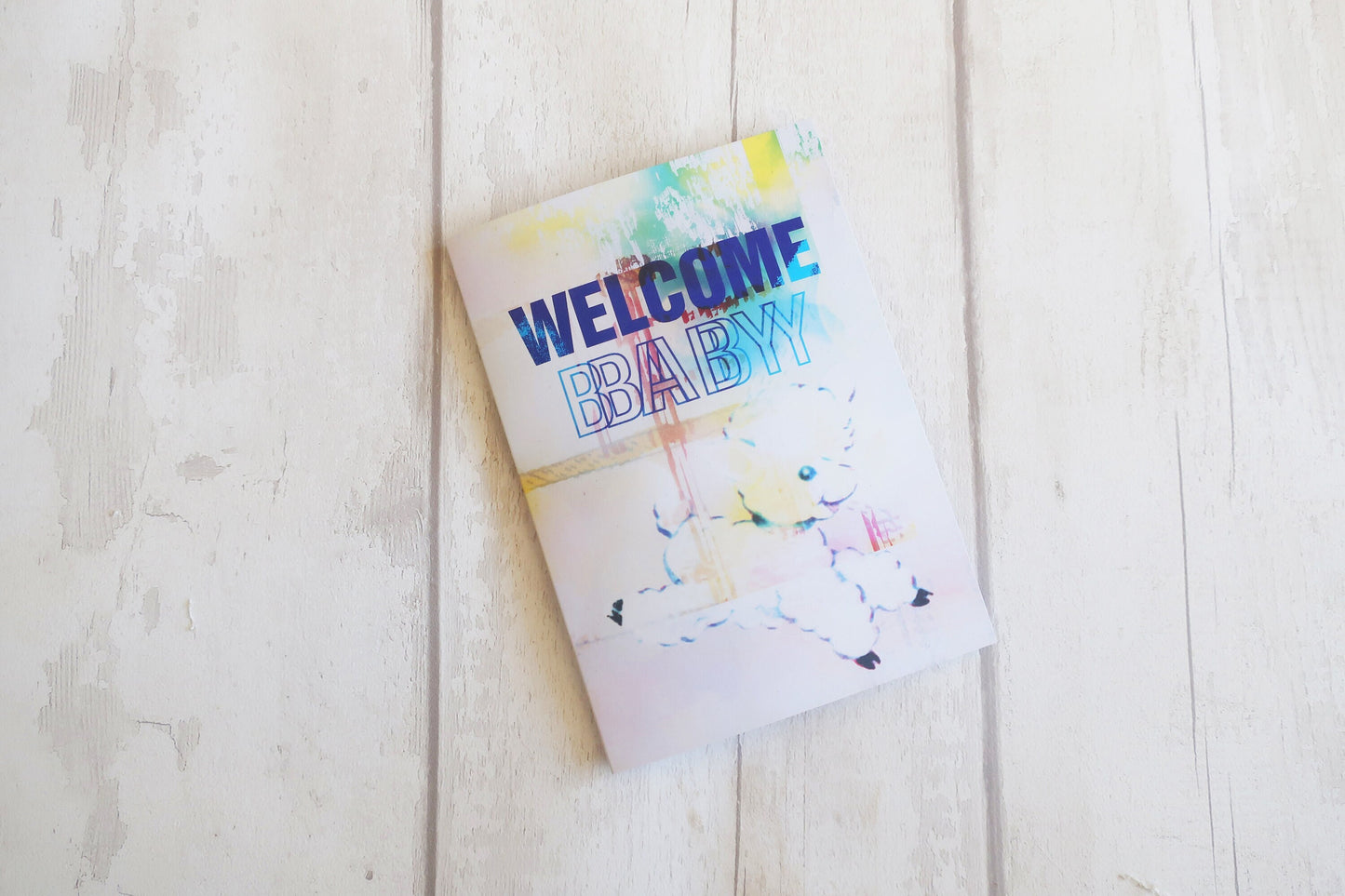 Greeting card with 'Welcome Baby' text on a light wooden surface
