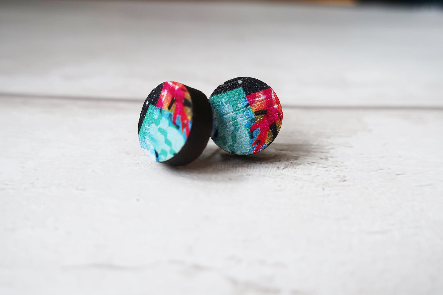 Colorful tie-dye patterned earrings on a light wooden surface
