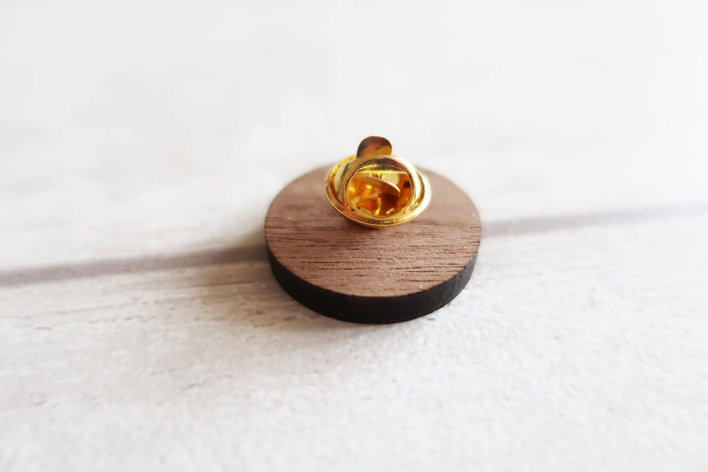 Gold clasp on a wooden pin badge back with a white background