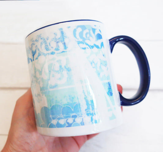 White mug with blue floral pattern held by a hand against a white background