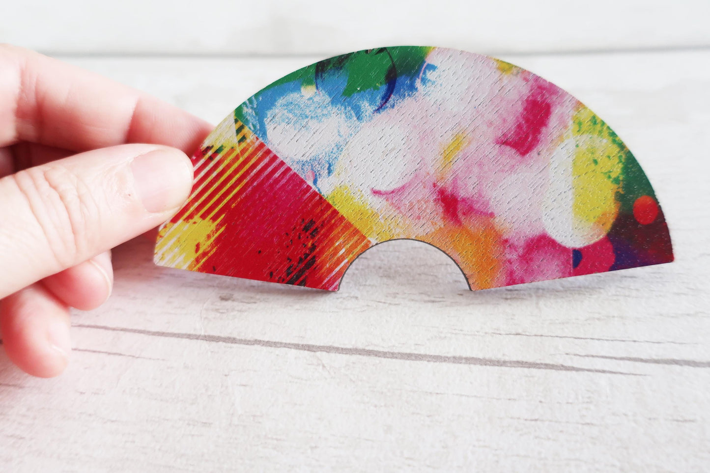 Colorful fan-shaped hairclip held by a hand on a light wooden surface
