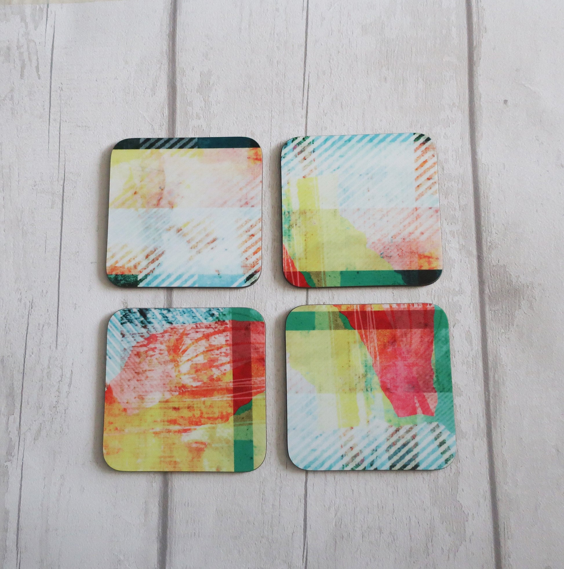 Four colorful square coasters on a light wooden surface