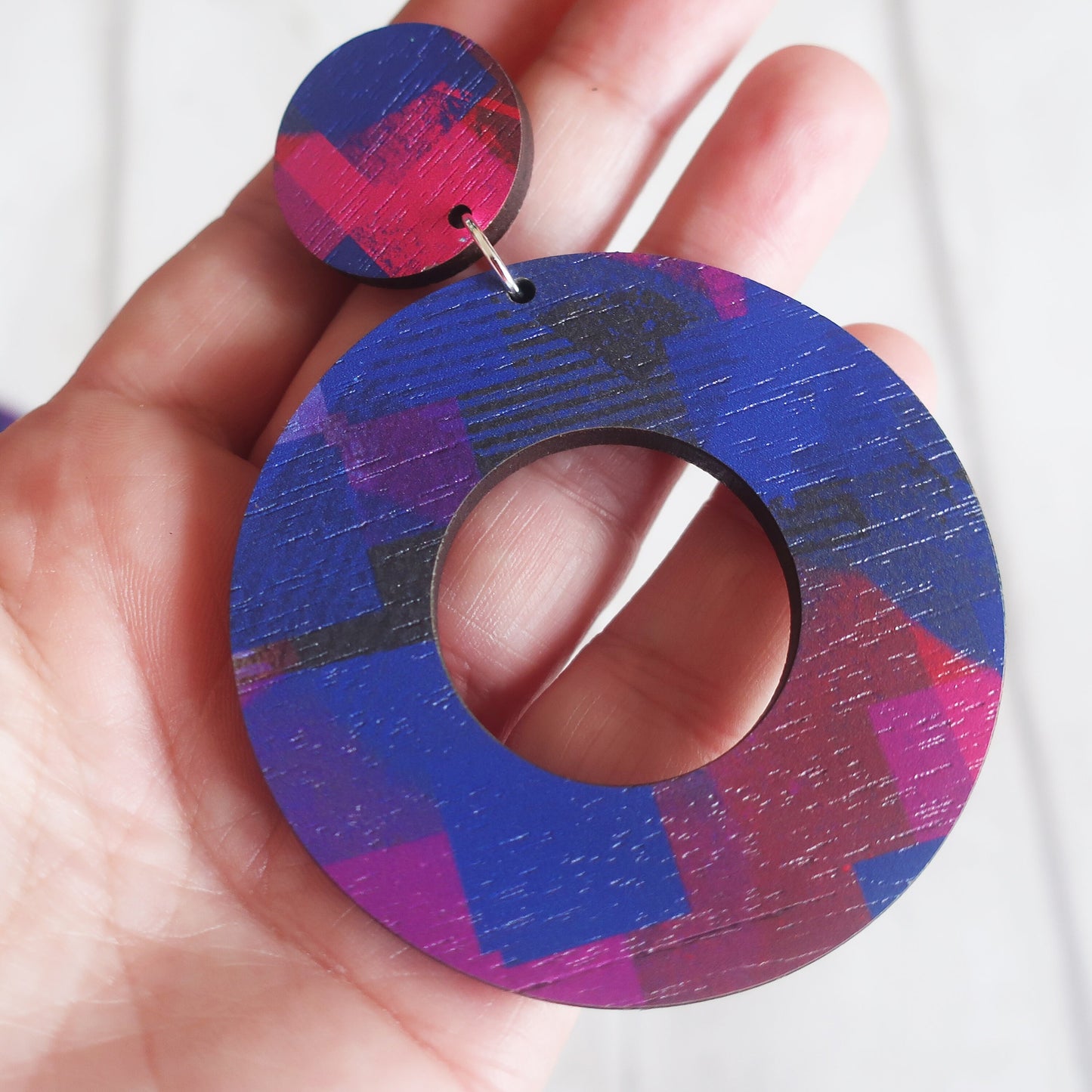 Colorful circular earrings held in a hand against a white background