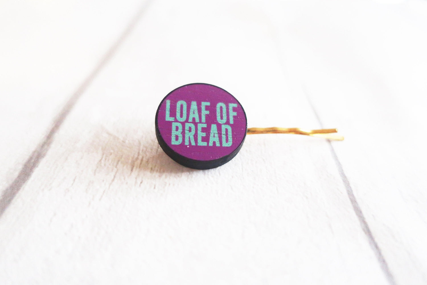 Purple hairclip with 'LOAF OF BREAD' text on a white surface
