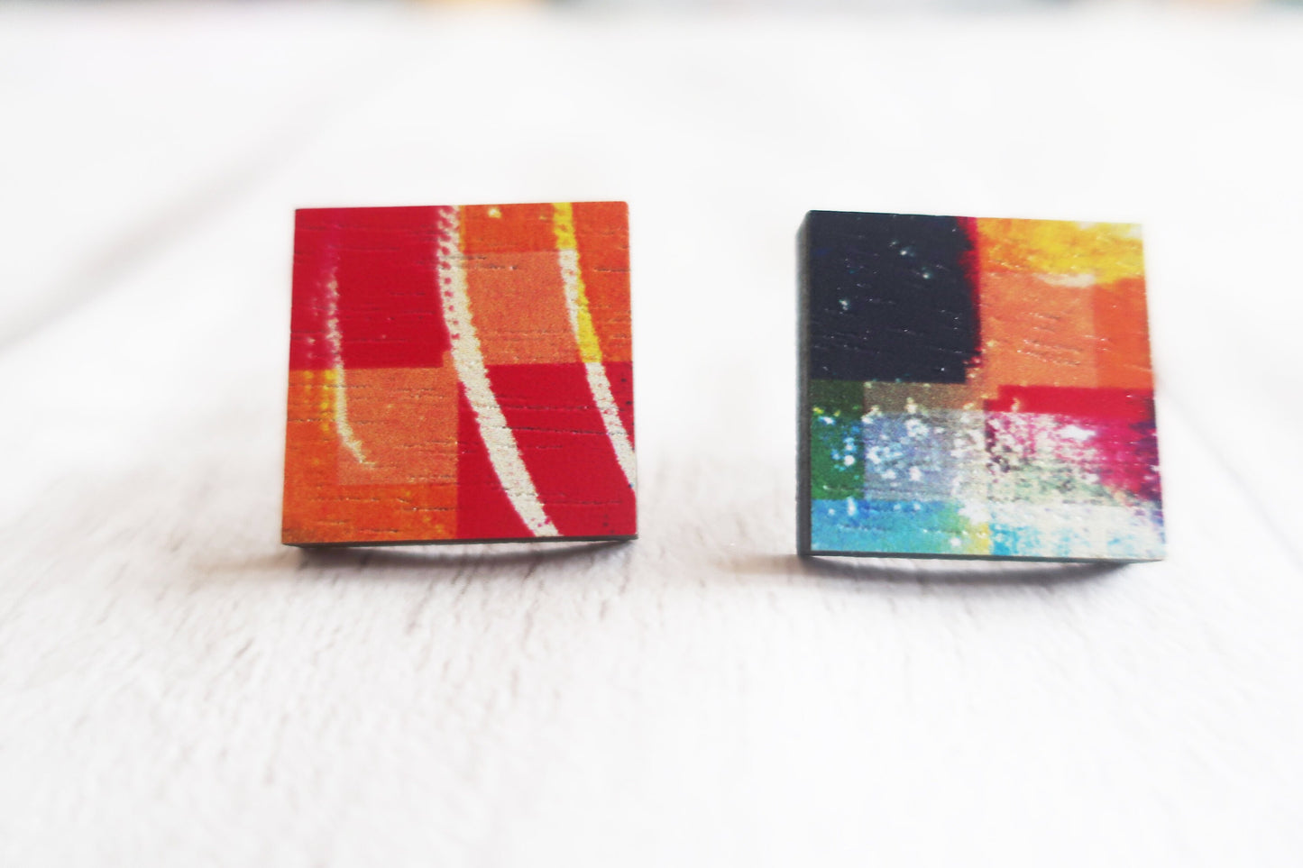 Two small square earrings with colorful abstract designs on a white background.