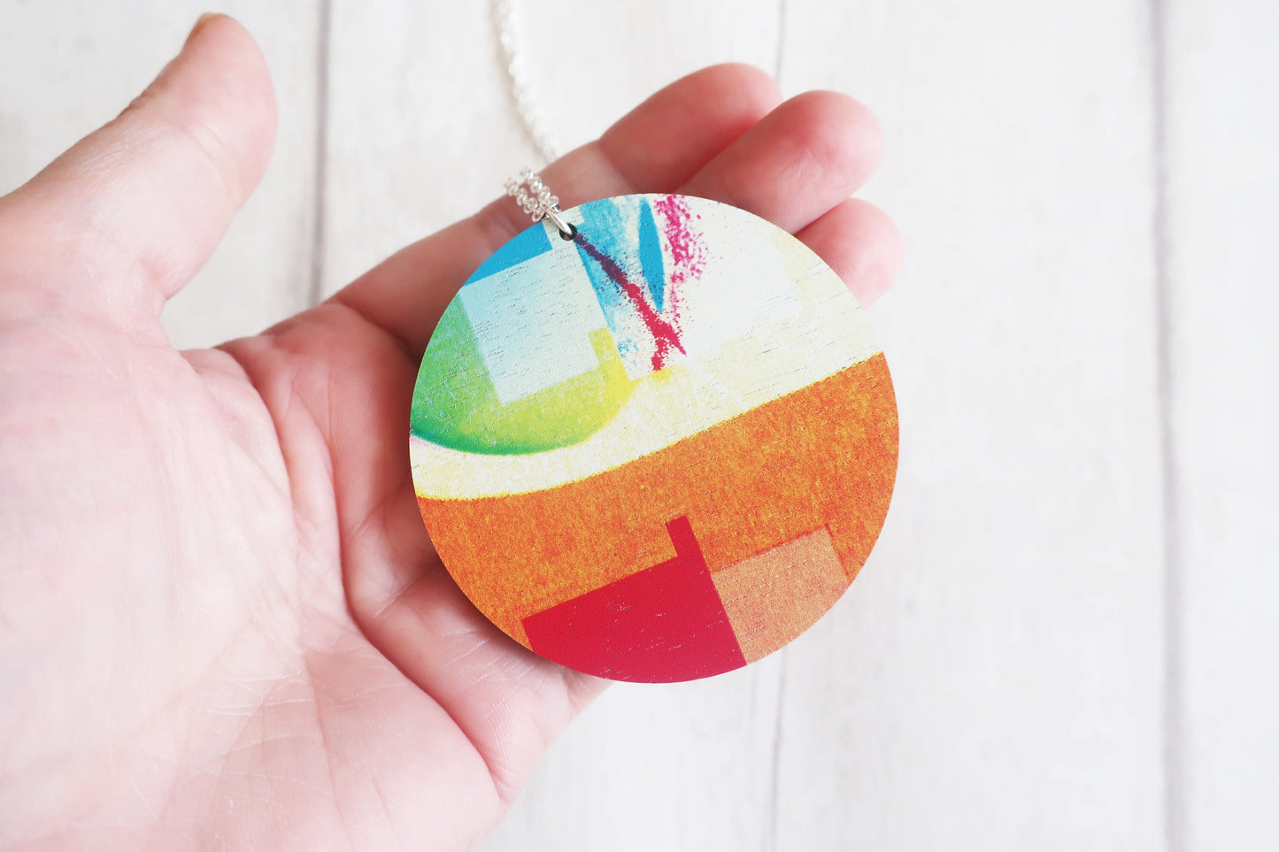 Colorful circular pendant held in a hand against a white background