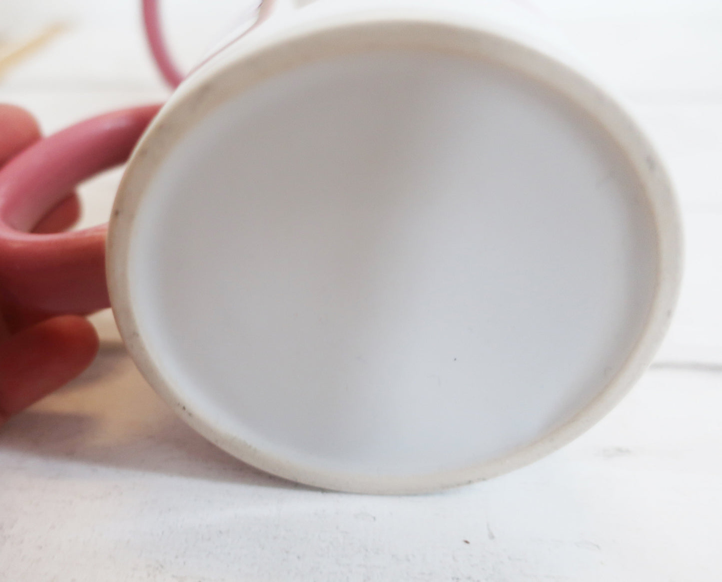 White ceramic mug bottom held by a hand on a light background