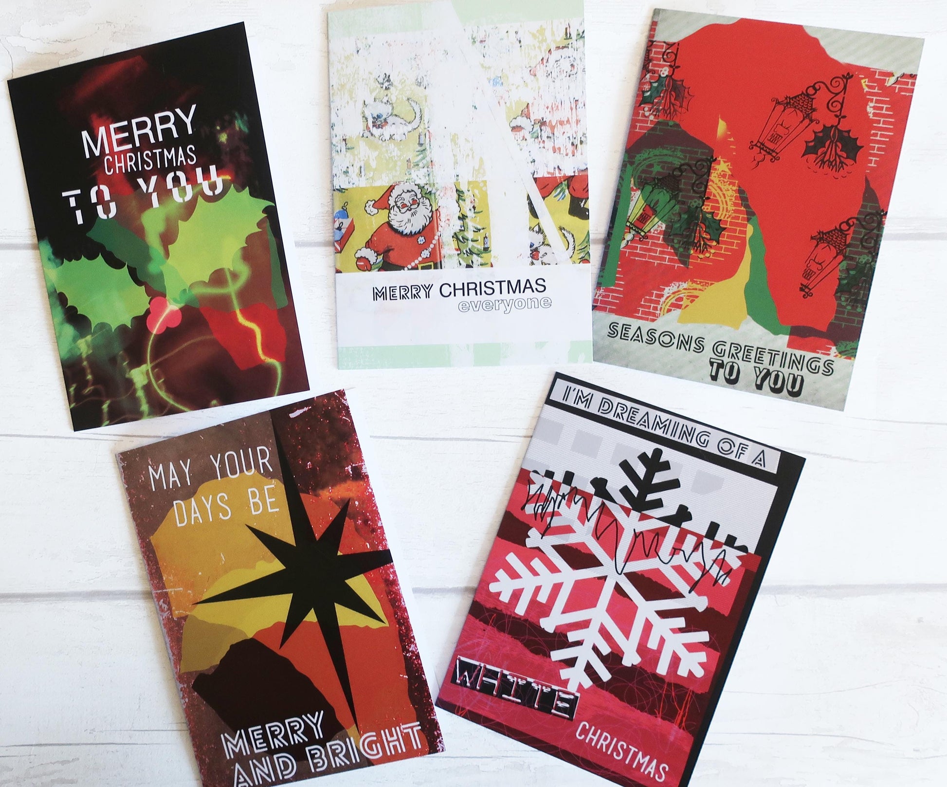 Five Christmas-themed greeting cards on a white wooden surface