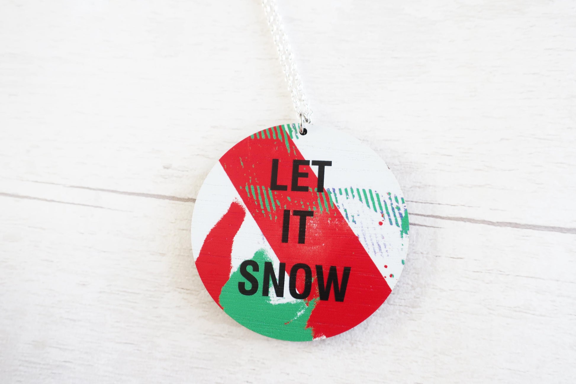 Round decorative necklace  with 'LET IT SNOW' text on a white background