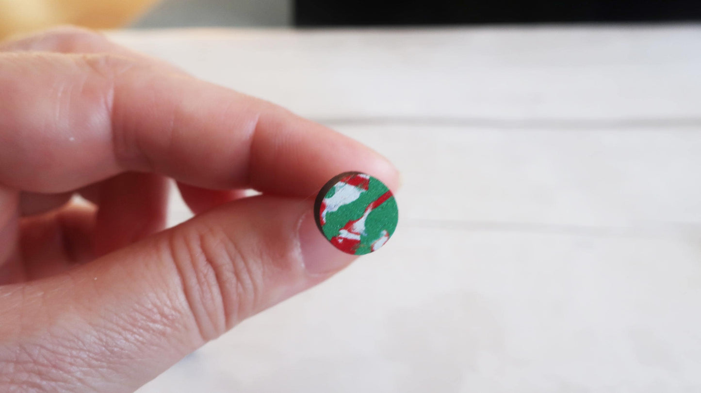 Small round earring with a design held between fingers against a white background