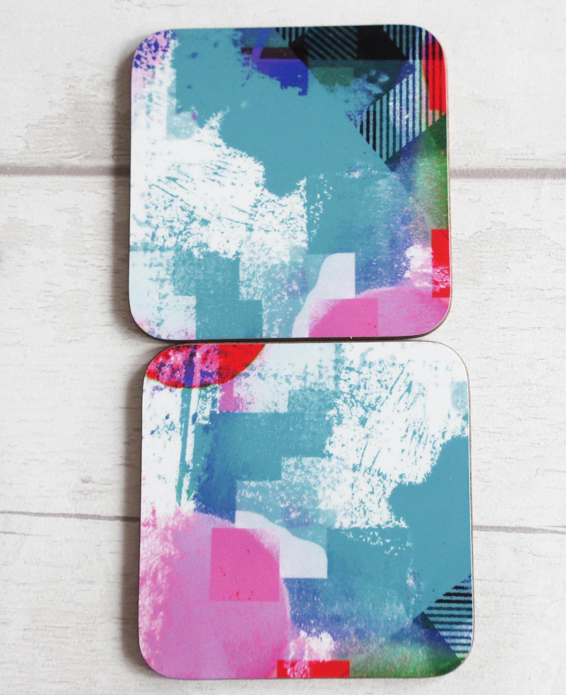 Two abstract art coasters with colorful patterns on a light wooden surface