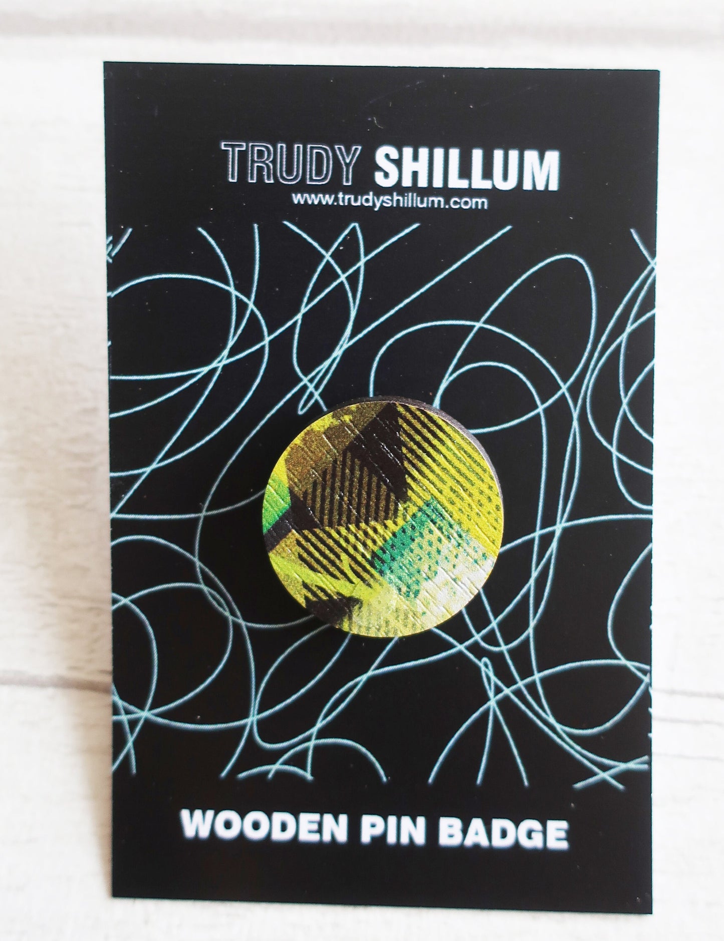 Trudy Shillum wooden pin badge on a black card with abstract designs