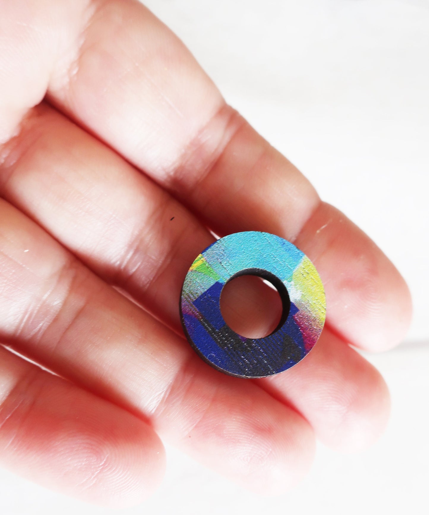 Colorful circular earring  held between fingers against a white background