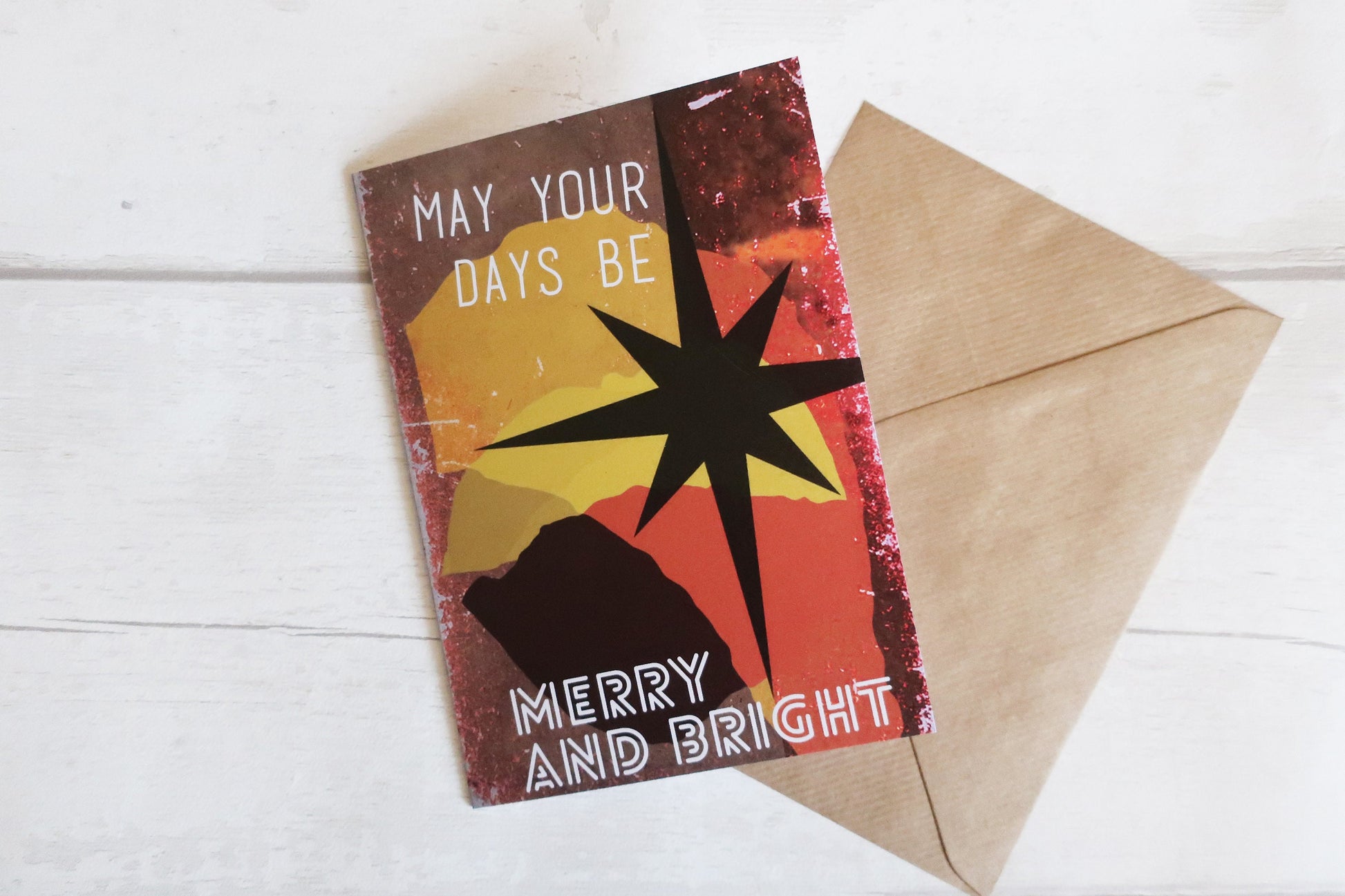 Greeting card with star design and text 'May your days be merry and bright' on a white wooden surface.