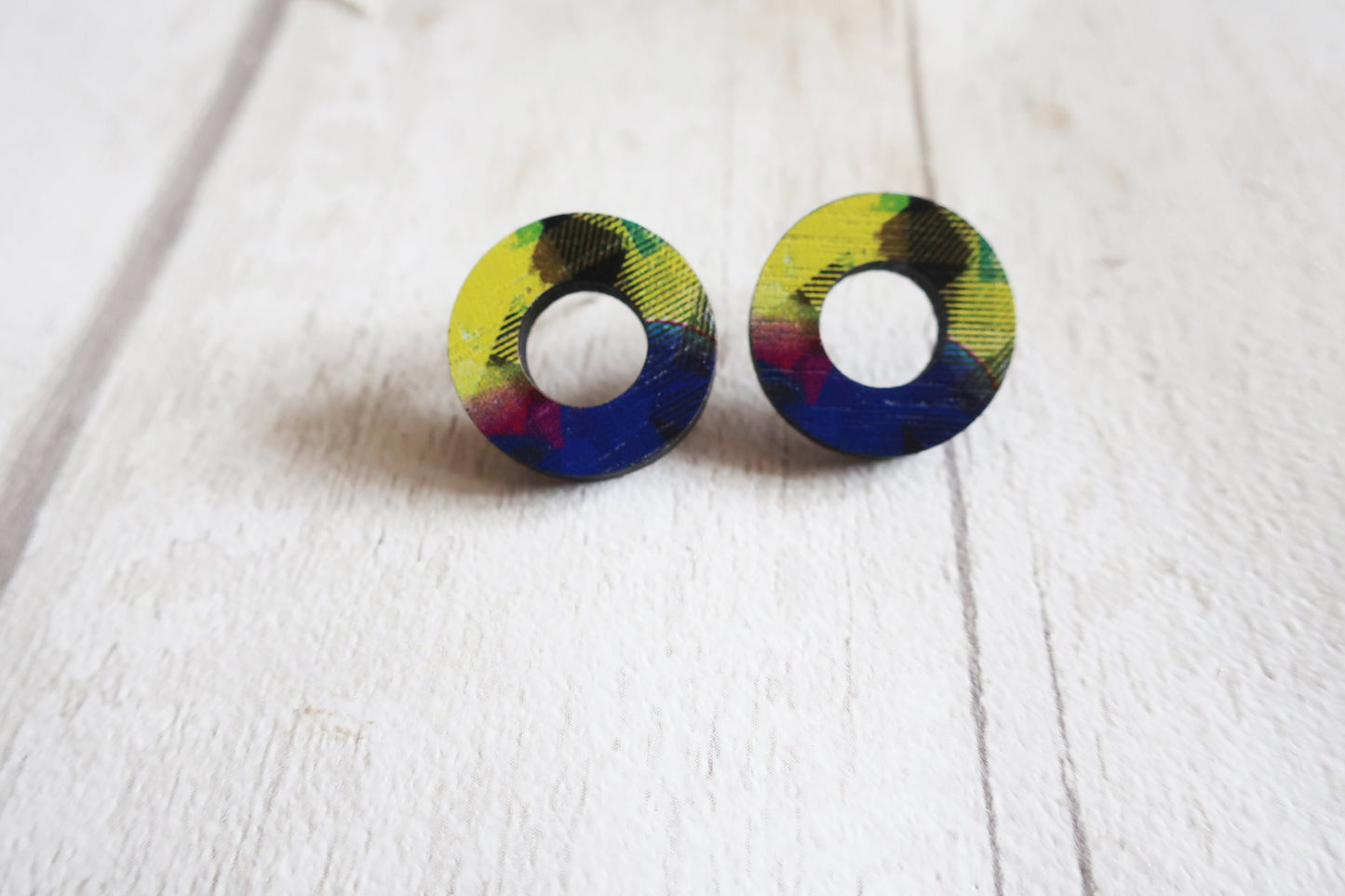 Pair of round earrings with multicolored design on a white wooden surface