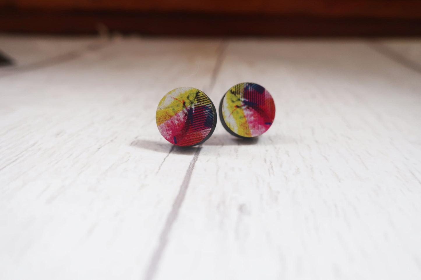 Colorful tie-dye patterned earrings on a light wooden surface