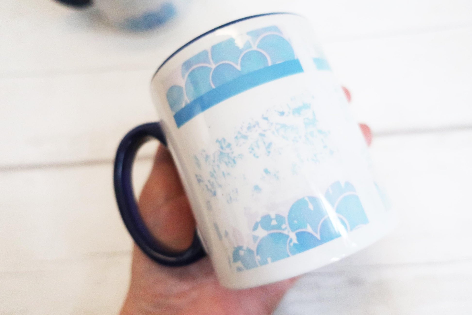 Mug with blue pattern held by a hand on a white surface