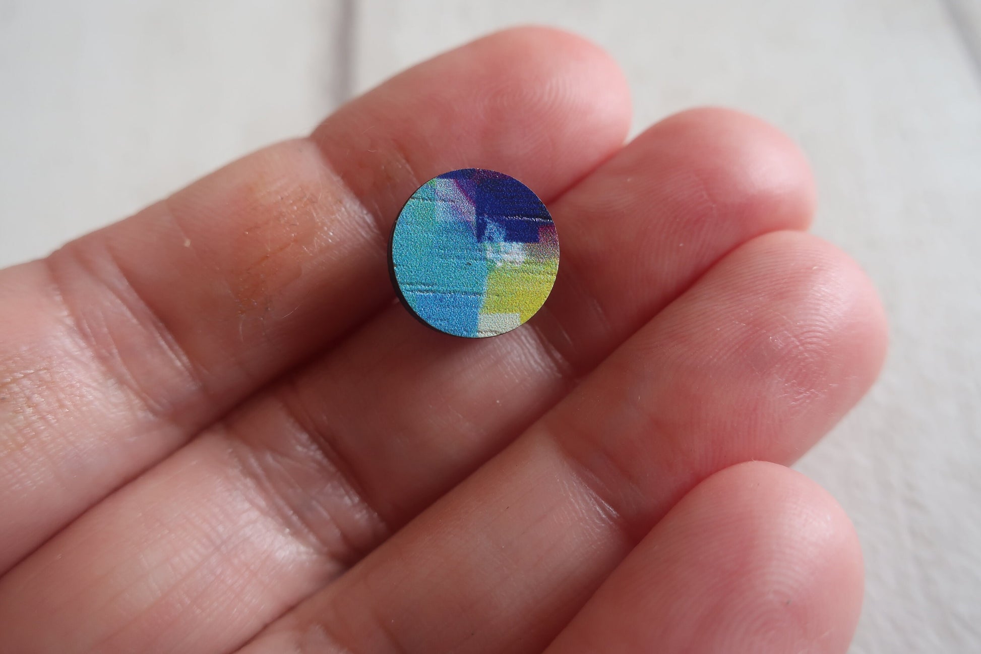 Colorful circular earring held between fingers against a neutral background