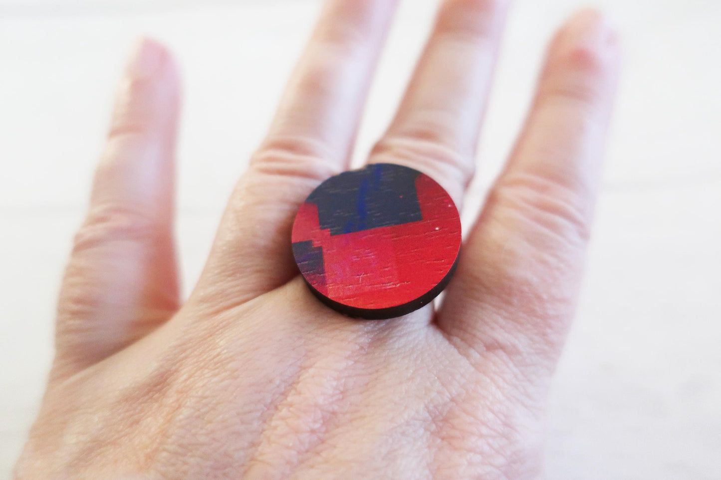Hand wearing a red and blue ring with a geometric pattern on a white background